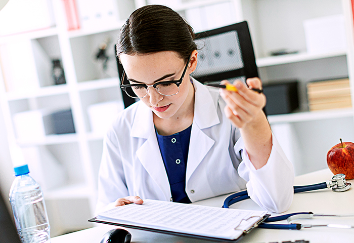 A beautiful young girl in a white robe is sitting at a computer desk with documents and a pen in her hands. A beautiful young girl in a white robe is sitting at a computer desk with documents and a pen in her hands.